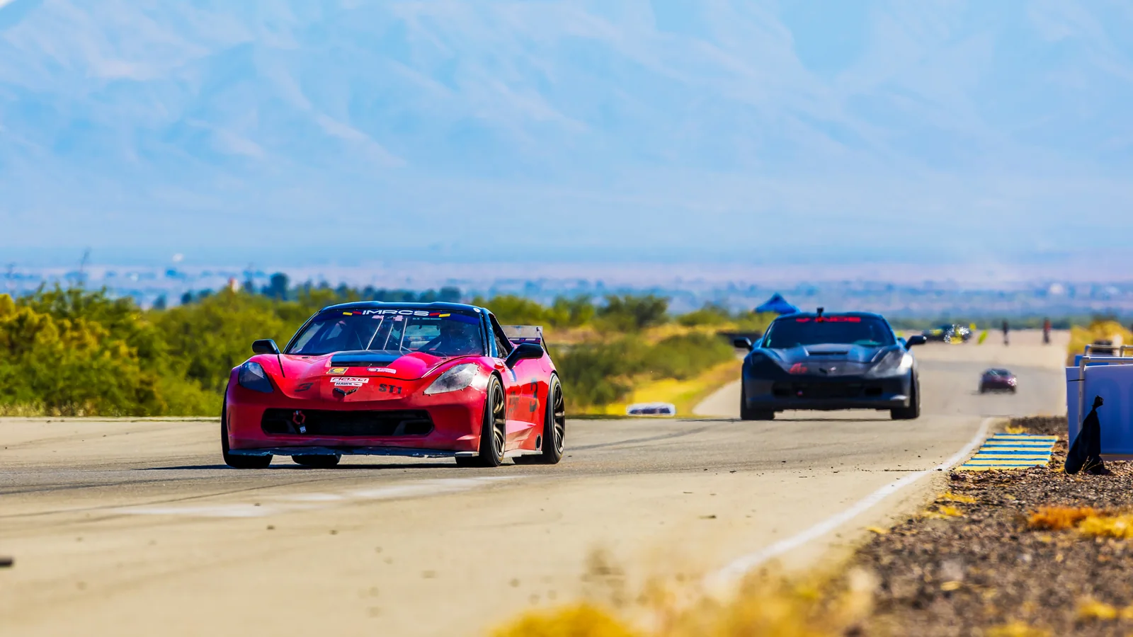 Red and black Corvettes racing with mountains in the background