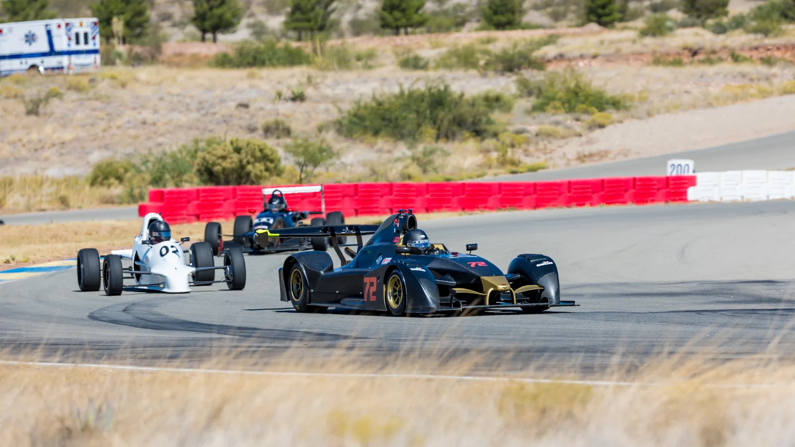 Three open-wheel race cars rounding a corner at INDE